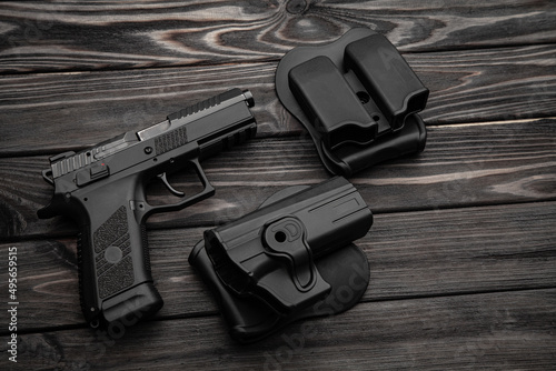 Pistol and plastic holster on a wooden back. A short-barreled weapon and a flashlight near the tactical backpack.
