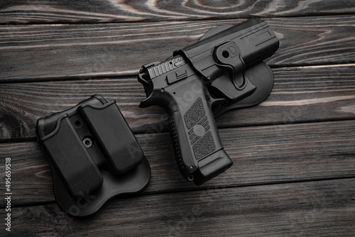 Pistol and plastic holster on a wooden back. A short-barreled weapon and a flashlight near the tactical backpack.