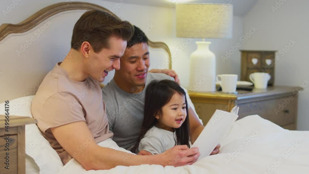 Family with two fathers in bed at home reading story to daughter together - shot in slow motion Family with two fathers in bed at home reading story to daughter together - shot in slow motion