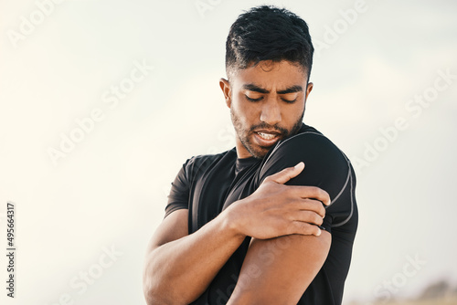 Injury will curtail any workout. Cropped shot of a handsome young male athlete holding his shoulder in pain while exercising on the beach. photo