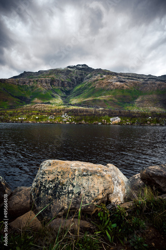 Vertical shot of a high hill covered with greenery on the coast of the lake against a cloudy sky photo