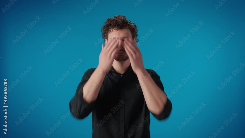 Portrait shocked male closed eyes by hands hiding having problem failure posing isolated on blue Portrait shocked male closed eyes by hands hiding having problem failure posing isolated on blue
