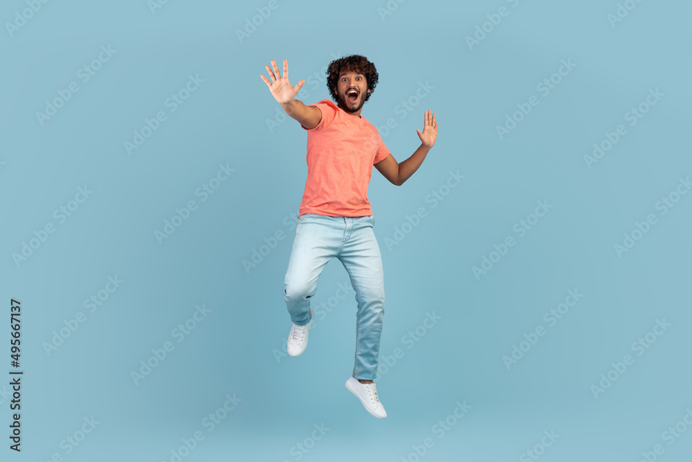 Carefree young indian man jumping over blue