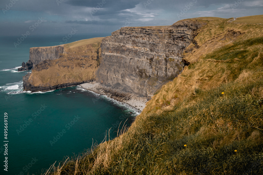 The Cliffs of Moher in Ireland's County Clare on a clear, sunny day at sunset. Burren, UNESCO Geopark, tall cliffs, Europe, Wild Atlantic Way, Atlantic Ocean, Doolin, Liscannor, grass, rock.