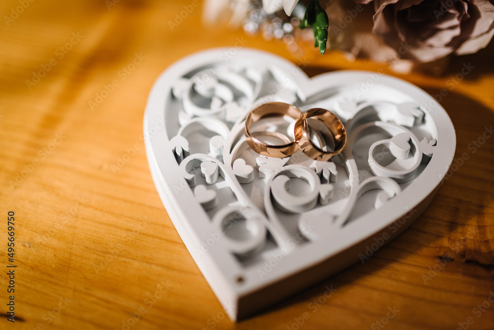 Two gold wedding rings on a wooden box in the shape of a heart. Top view. Wedding rings of the bride and groom. Engagement. Two gold wedding rings on a wooden box in the shape of a heart. Top view. Wedding rings of the bride and groom. Engagement.