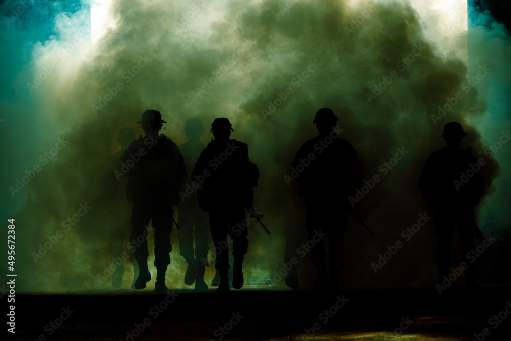 silhouette group of thai soldiers special forces full team in uniform walking action through smoke and holding gun on hand and over the lighting background.