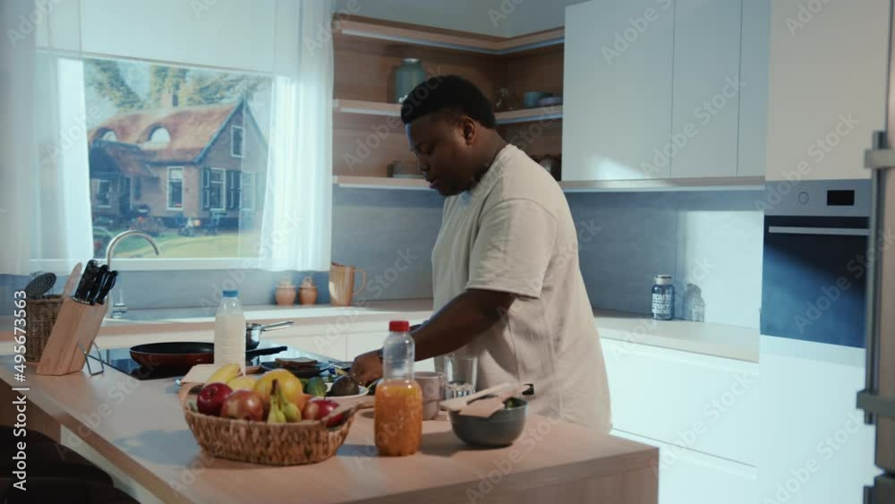 Funny african american young man moving in rhythm in the kitchen while cooking. Amusing energetic guy listening to music and dancing at home kitchen.