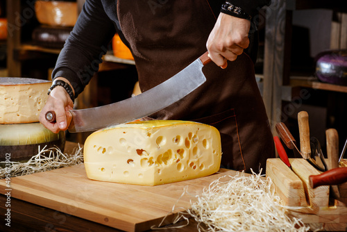 Tablou pe pânză chef cuts hard cheese with special cheese knife, cheese sale concept