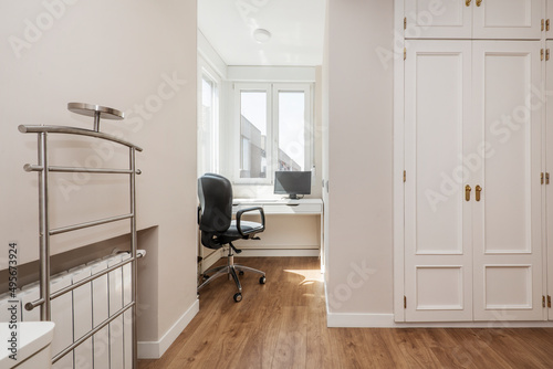Bedroom with white wooden desk with black swivel office chair, white wooden built-in wardrobe and stainless steel vanity