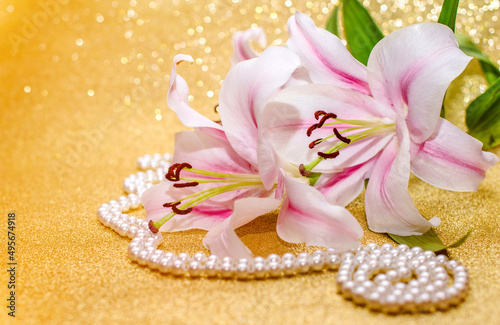 White lilies and pearl necklace on a shiny gold background 