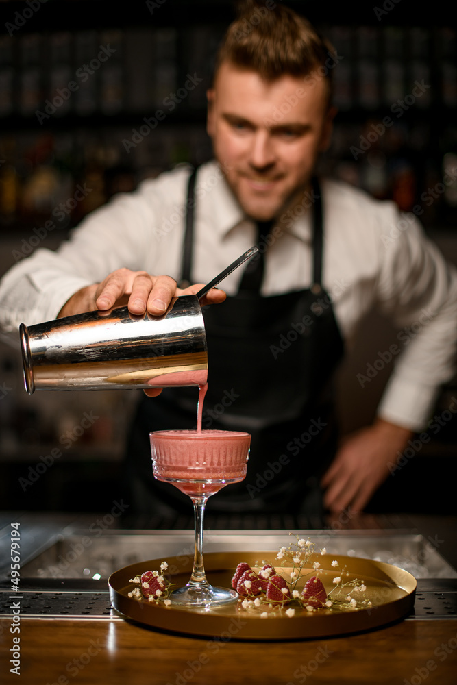 hand of bartender pours cocktail from shaker into crystal glass stands on round tray hand of bartender pours cocktail from shaker into crystal glass stands on round tray