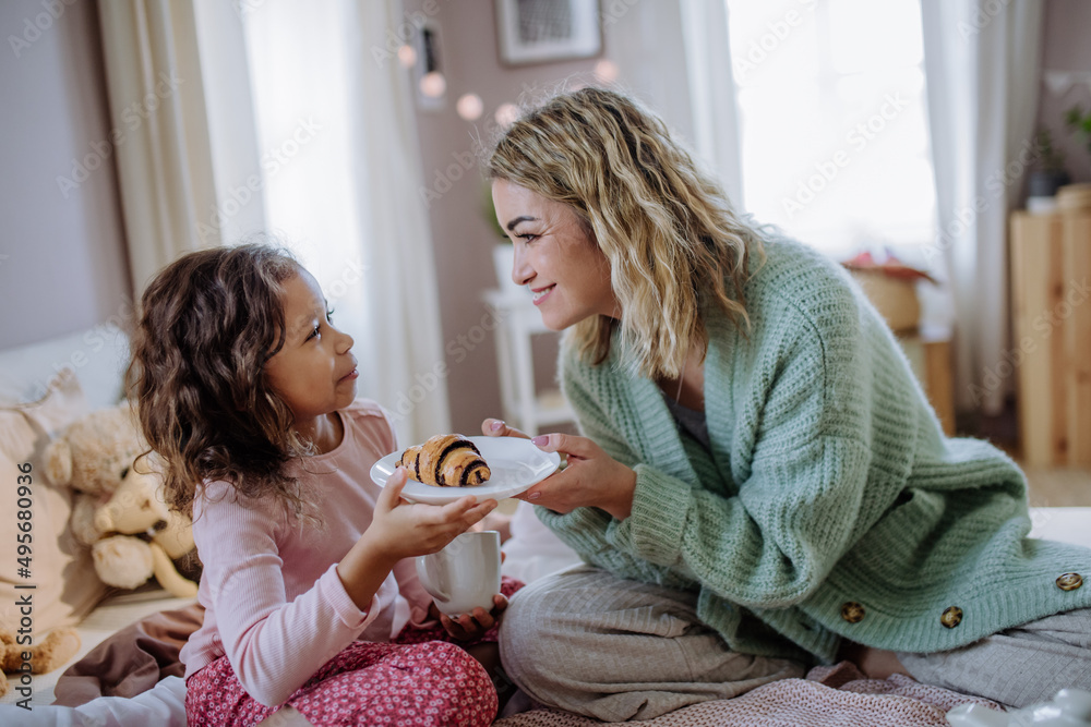 Happy mother with her little daughter having breakfast together in bed at home.