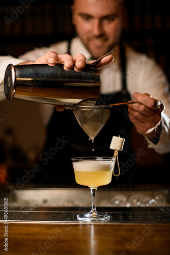 hands of bartender gently strain the cocktail through a sieve into a glass