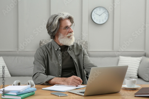 Middle aged man with laptop and notebook learning at table indoors
