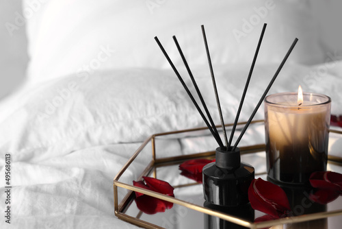 Aromatic reed air freshener, red petals and candle on bed, space for text