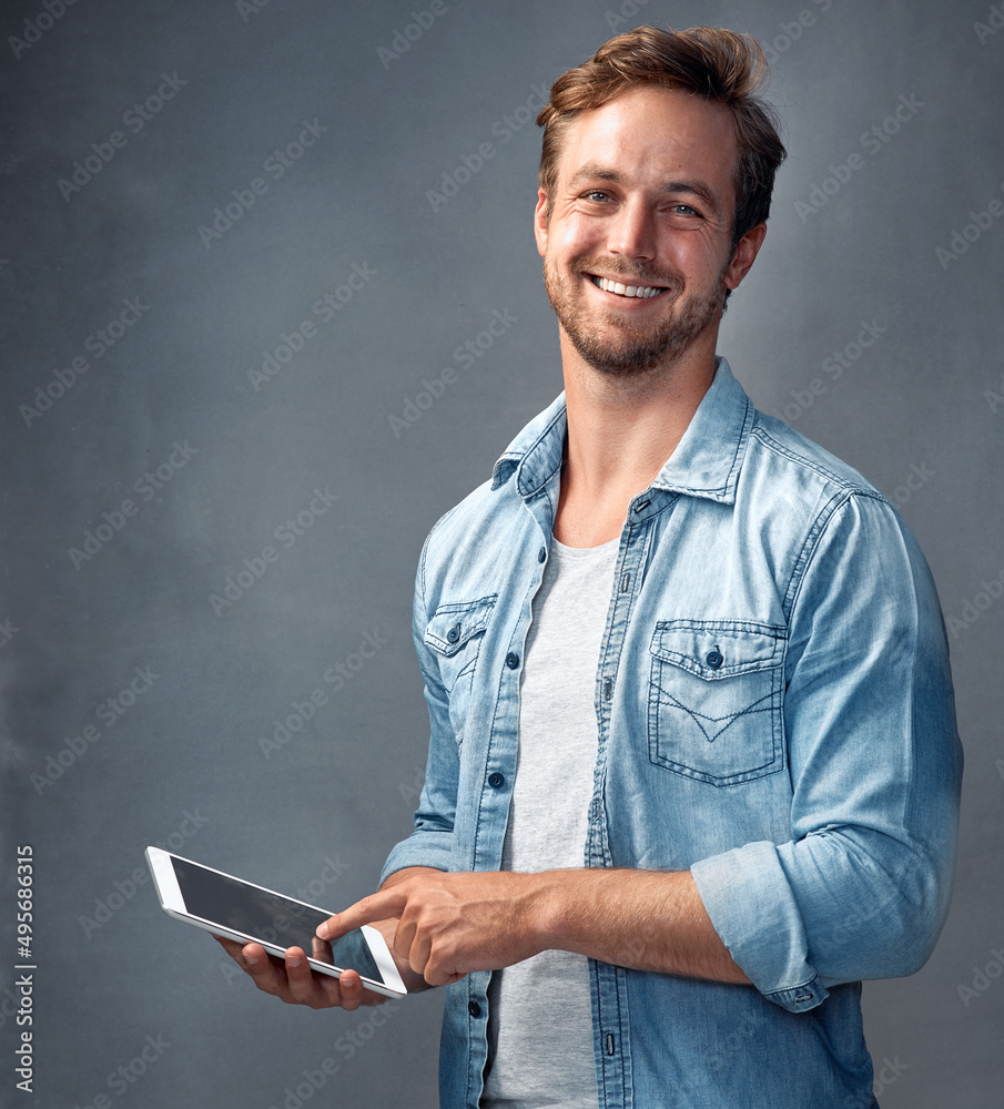 Keeping things social online. Portrait of a handsome young man using a tablet against a gray background in the studio. Keeping things social online. Portrait of a handsome young man using a tablet against a gray background in the studio.