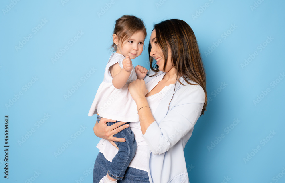Photo of pretty young mommy hugging little daughter standing isolated over blue background. Motherhood concept. Photo of pretty young mommy hugging little daughter standing isolated over blue background. Motherhood concept.