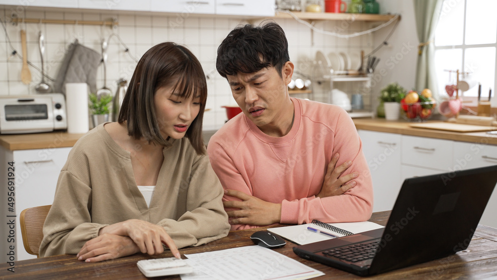 stressed Asian young couple making budget plan for mortgage loans bill. the husband folds arms as his wife is showing him figure on the calculator and bills stressed Asian young couple making budget plan for mortgage loans bill. the husband folds arms as his wife is showing him figure on the calculator and bills