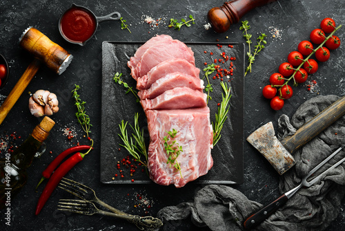 Raw pork fillet with spices on a black stone background. Meat. Top view. Rustic style. photo