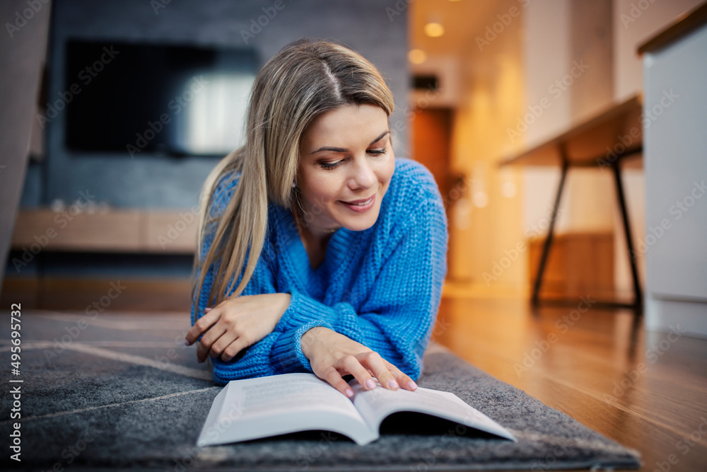 A happy woman lying on the floor and enjoying a book at her home. A happy woman lying on the floor and enjoying a book at her home.