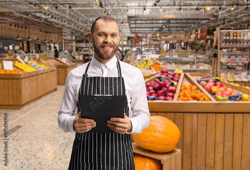 Male shop assistant in a grocery store holding a clipboard photo