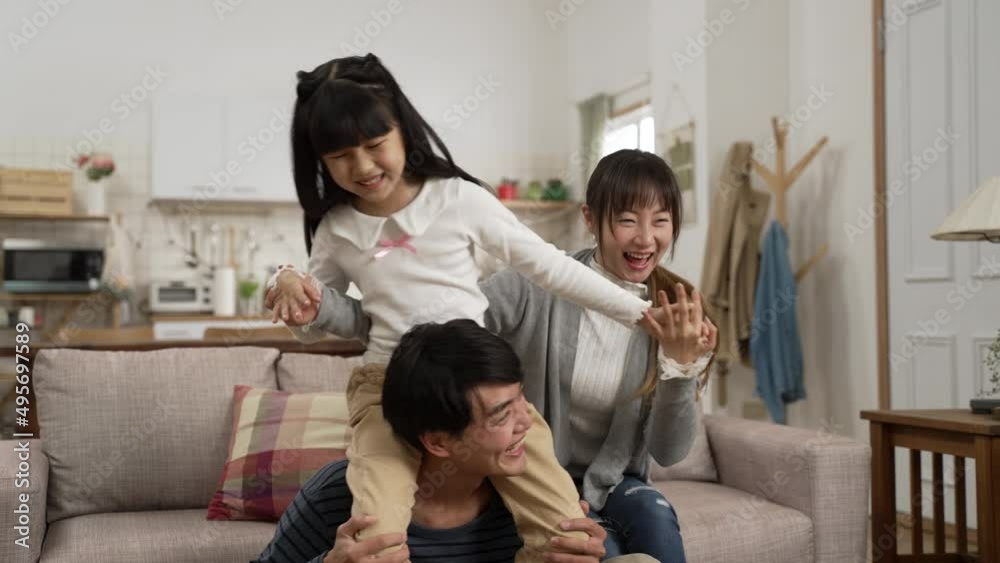 cheerful asian family of three playing together at home. the father carrying his daughter on shoulders while the mother is helping hold the girls’ hands
