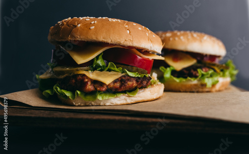 Delicious big juicy burger with tomatoes, cucumbers, cabbage, greens, cheese, cutlet on a gray background. Two sandwiches, fast food. Snack, appetizing, bun with sesame seeds. Serving in restaurant © lesia17