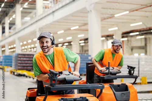 Two warehouse workers having fun at work by driving forklifts.