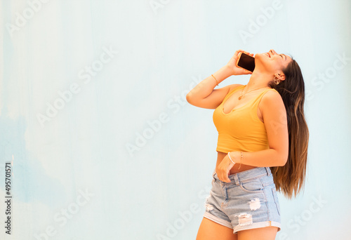 Mujer joven con teléfono móvil aislado sobre fondo gris con sorpresa y expresión facial conmocionada,short corto,pantalon corto,top,celular, photo