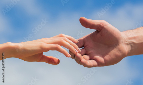 Giving a helping hand. Hands of man and woman on blue sky background. Lending a helping hand. Hands of man and woman reaching to each other, support. Solidarity, compassion, and charity, rescue © Yevhen