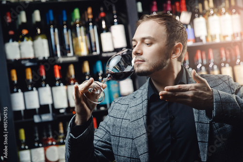 Portrait Sommelier holds glass with red wine in restaurant, tests aroma and color, dark background alcohol store