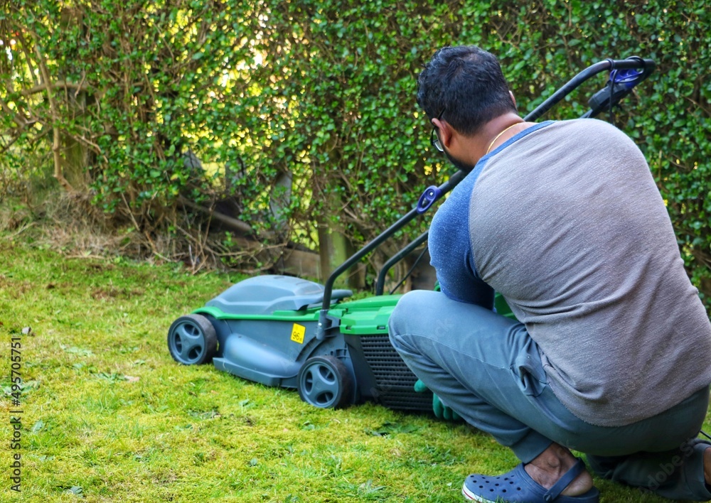 Fototapeta premium An unrecognizable asian indian man sitting on grass and adjusting the grass basket from a electric lawn mower machine.