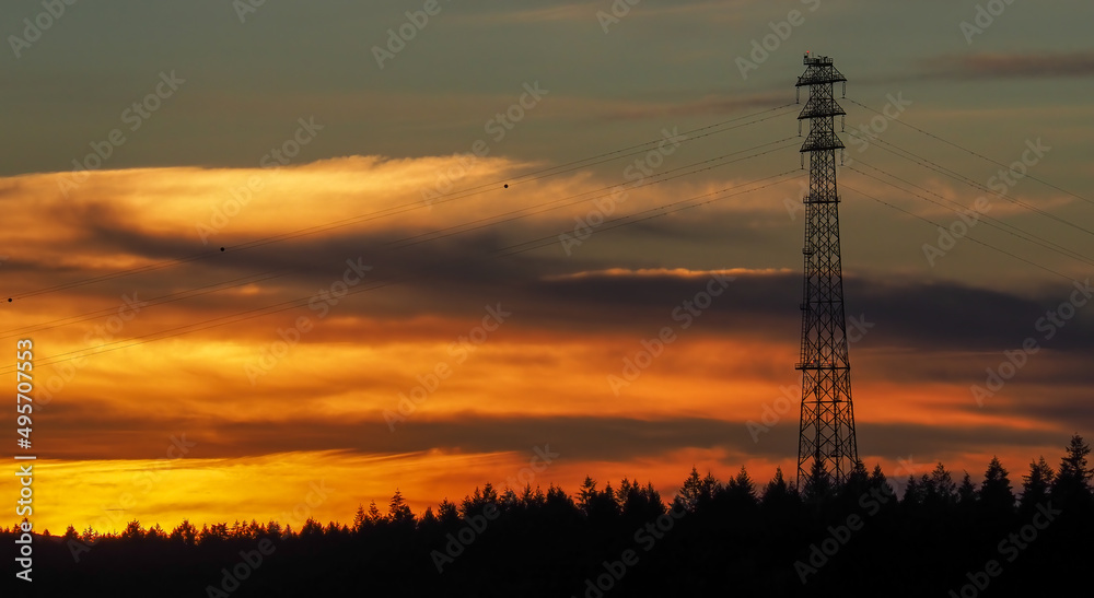 Dramatic sunset behind a very tall transmission tower and its associated power lines.