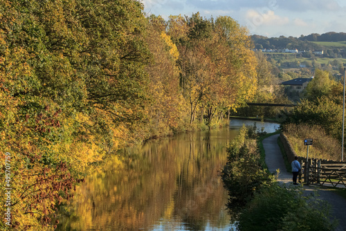 Fototapeta Naklejka Na Ścianę i Meble -  Autumn colours reflected in the Leeds and Liverpool Canal near Bingley with the towpath inviting walkers and hikers to enjoy a relaxing peaceful time close to nature
