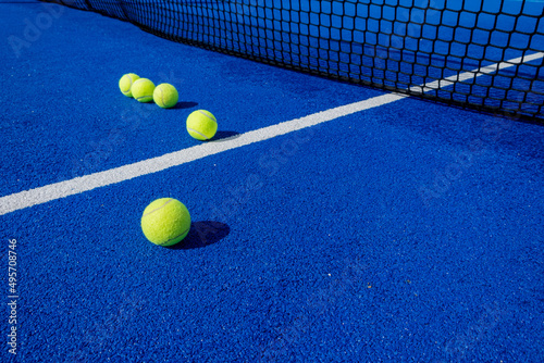 five paddle tennis balls and the net of a blue paddle tennis court, selective focus © Vic
