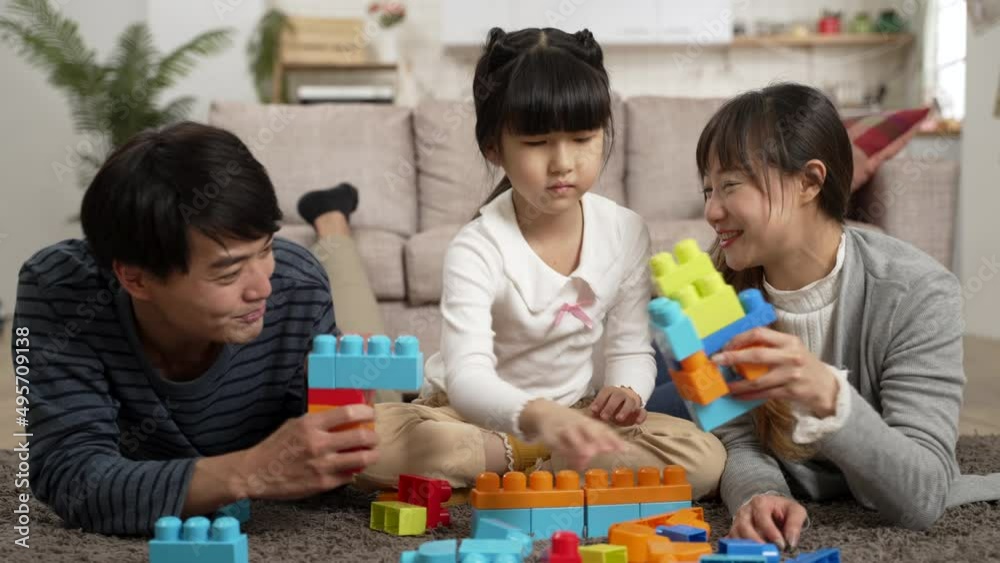 slow motion of childlike asian mom and dad playing fighting game with toy bricks. the annoyed daughter is building up her own work in the middle and pushing away the man’s hand slow motion of childlike asian mom and dad playing fighting game with toy bricks. the annoyed daughter is building up her own work in the middle and pushing away the man’s hand