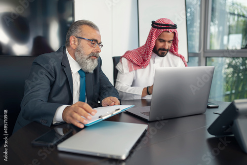 Business meeting in the office, Arabian businessman having a business conversation with a Mature businessman and working on the laptop 