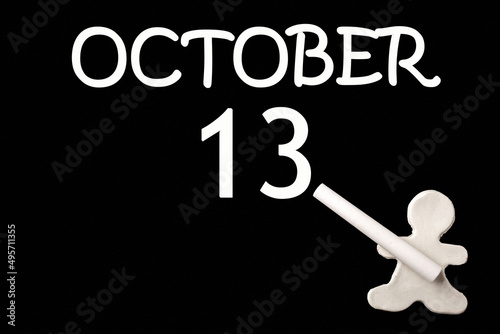 A small white plasticine man writing the date 13 October on a black board. Business concept. Education concept.