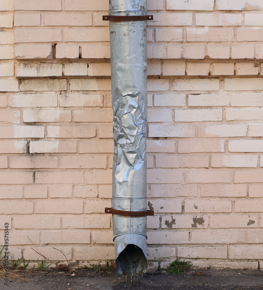 A crumpled gray metal downpipe on a pink brick wall