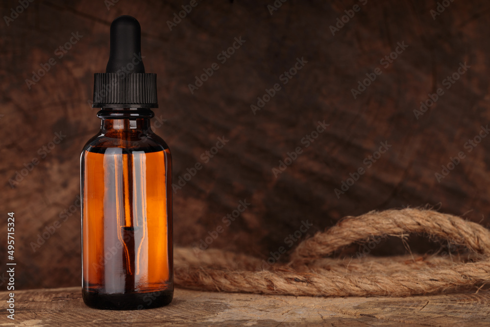 Fototapeta premium Glass cosmetic bottle on brown wooden background. Dropper bottle, cosmetic container dispenser flat layout. MOCK-UP.