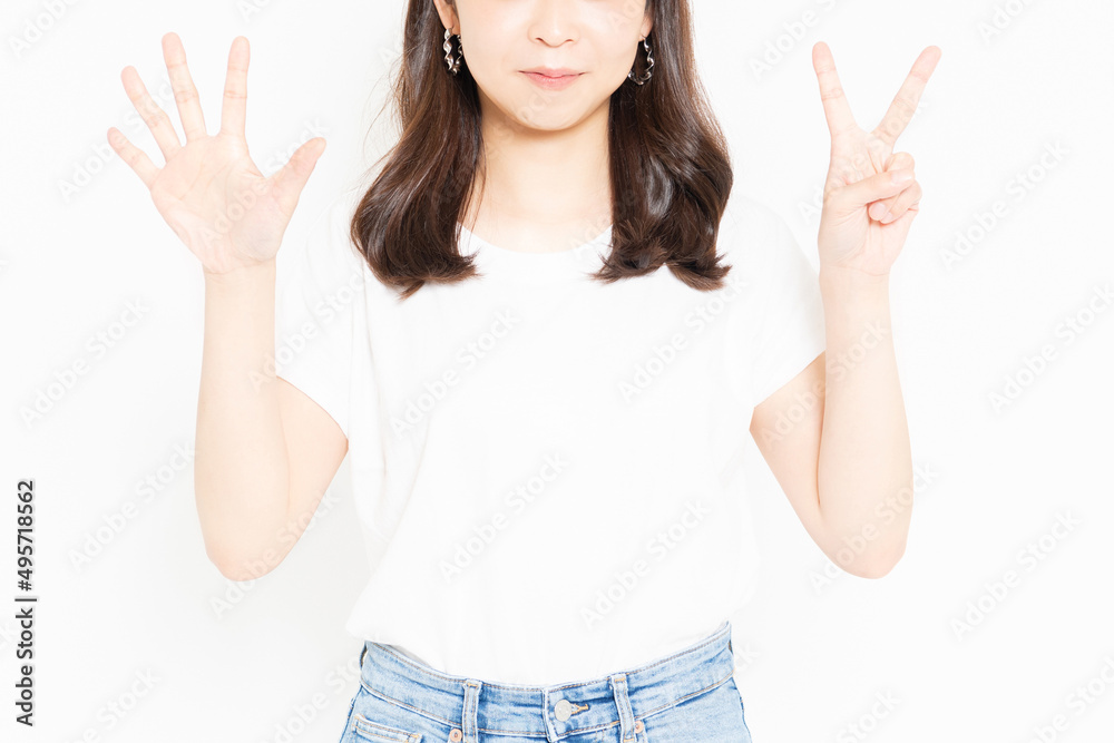 白い背景の前に立って、手で数字の7を表すTシャツを着ている若い女性