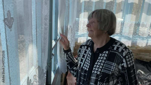 An old woman looks out the window of a country house in Ternopil region, Ukraine