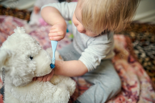 Fotografia little girl brushes her teeth with a soft toy teddy bear