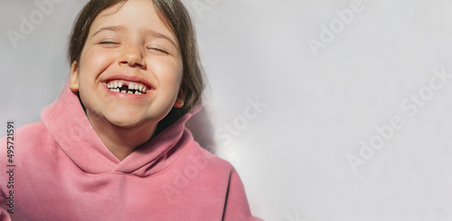 portrait of a beautiful emotional caucasian girl in a pink sweatshirt who lost her first tooth. Close-up of a child with a smile and joy