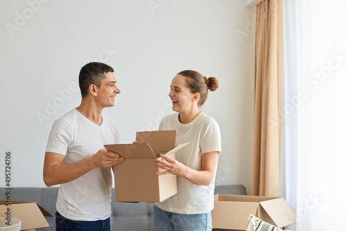Portrait of smiling happy young couple standing surrounded with carton boxes, family during relocation into a new apartment, looking at each other with smile. © sementsova321