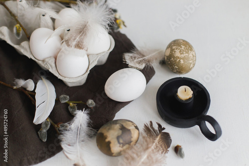 Easter natural eggs in tray, feathers, willow branches, nest on linen napkin on white wooden table. Easter rustic still life. Simple Easter aesthetics in pastel brown colors. Happy Easter