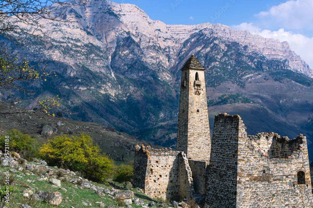 An ancient stone tower with a religious symbol in the form of a man.  An old medieval tower for watching enemies against the background of mountains.