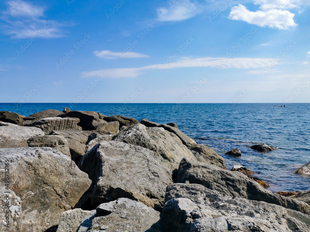 Large stones on the seashore on the background a blue sky with white clouds. Large stones on the seashore on the background a blue sky with white clouds.The Ligurian Sea, Italy.