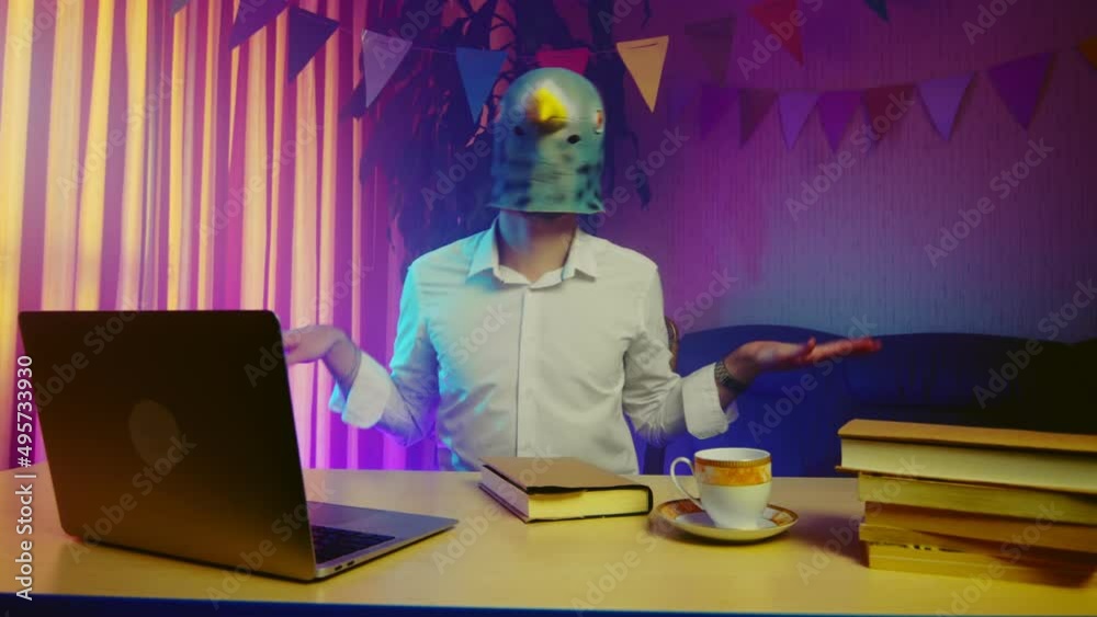 A young man in a pigeon mask sits on a chair and imitates the flight of a bird. Multicolored lighting. Masquerade A young man in a pigeon mask sits on a chair and imitates the flight of a bird. Multicolored lighting. Masquerade