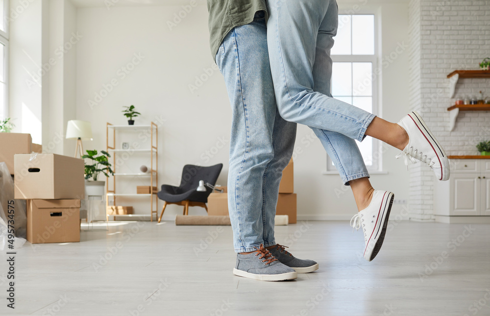 Happy people enjoying romantic moment in new home. Married couple kissing while unpacking in new house or studio flat, cropped low section shot of man's and woman's legs. Buying real estate concept Happy people enjoying romantic moment in new home. Married couple kissing while unpacking in new house or studio flat, cropped low section shot of man's and woman's legs. Buying real estate concept